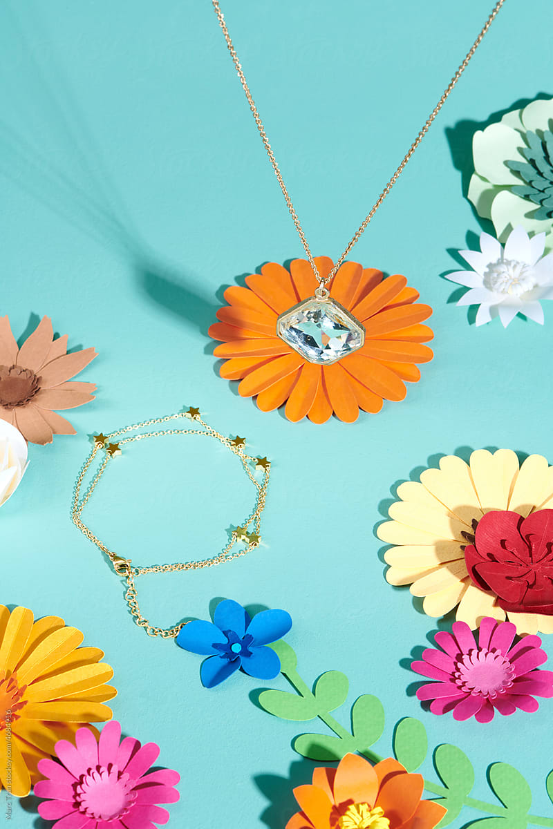 A set of gold necklace and bracelet on the table with paper flowers