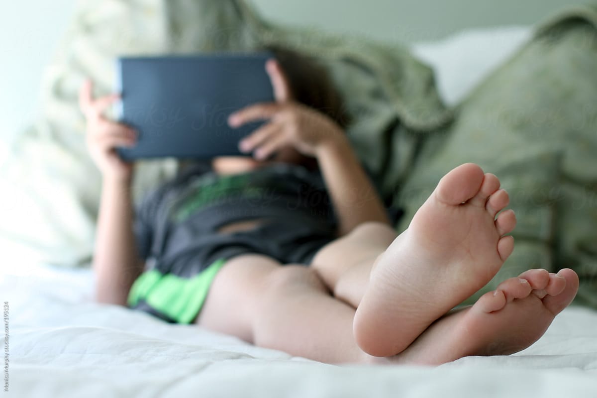 Young child lounges and plays on  his electonic tablet