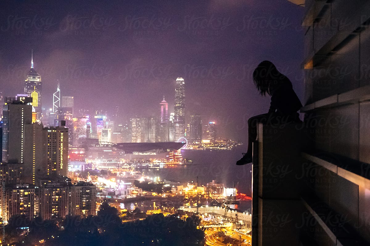 Girl sits on edge of a building rooftop overlooking hong kong