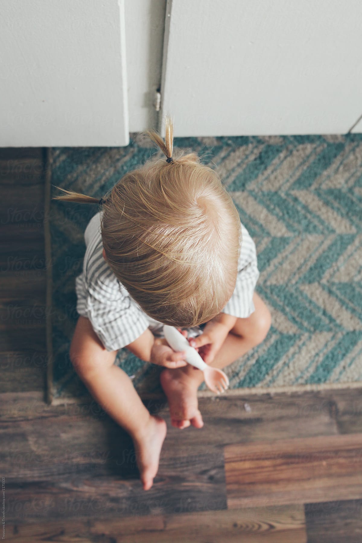Toddler sitting on kitchen floor holding a spoon