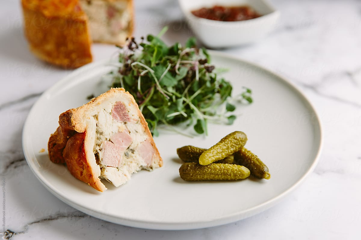 A raised chicken and ham pie with salad and pickles.