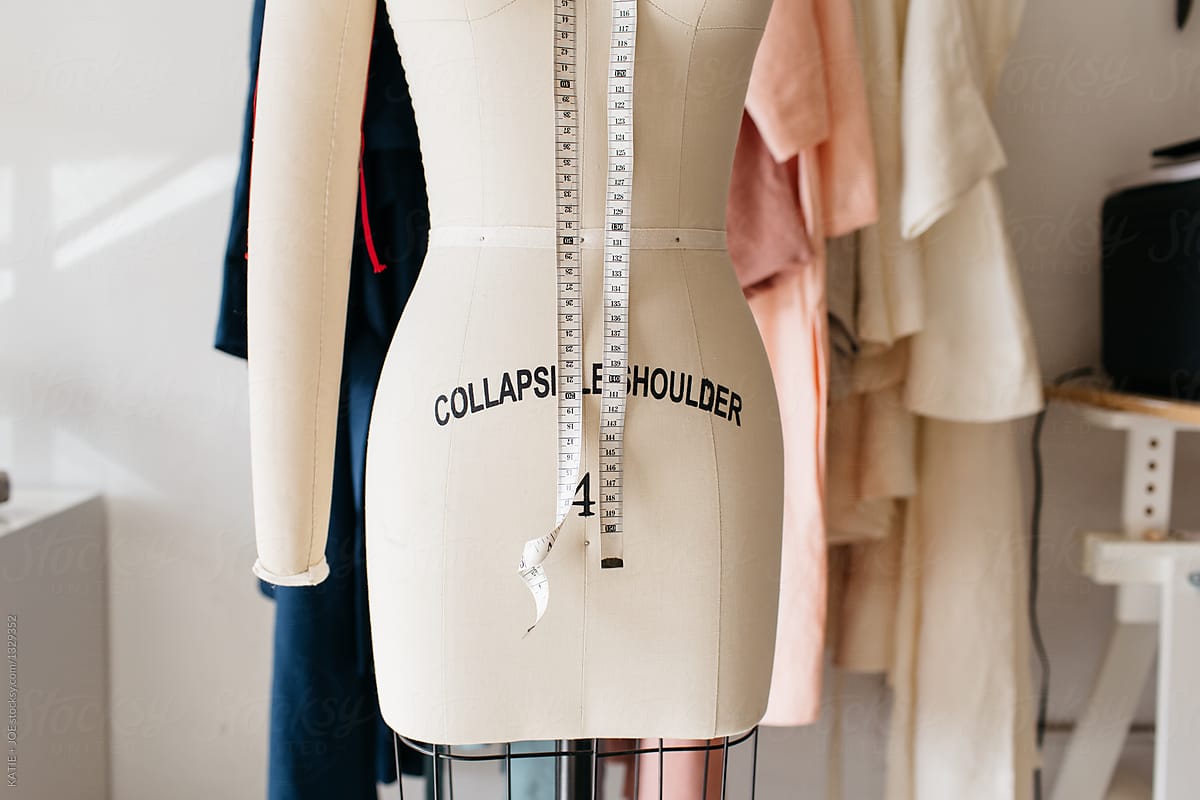 mannequin dress form with measuring tape in front of clothing rack