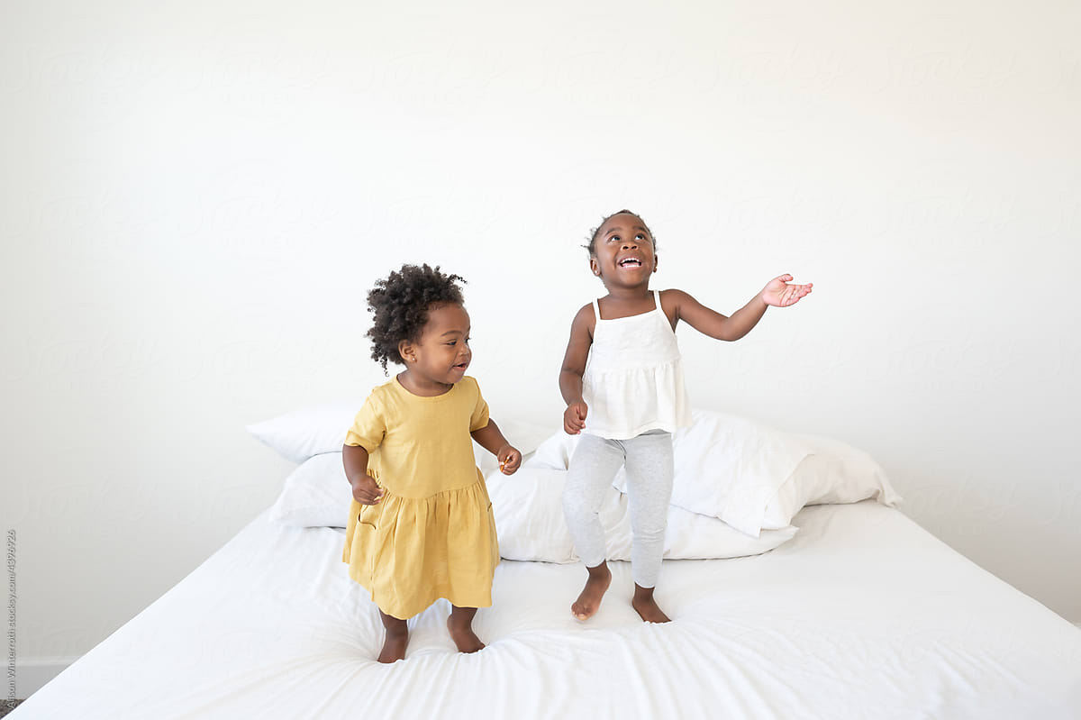 Two toddlers jumping on a bed