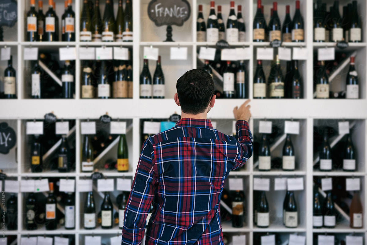 Wine: Man Stands In Front Of Wall Of Wine Choices