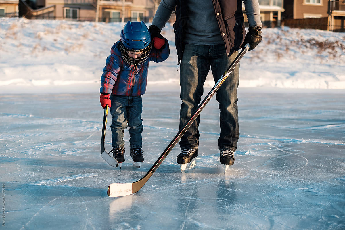 A father holds his son\'s hand as they skate on a frozen pond.