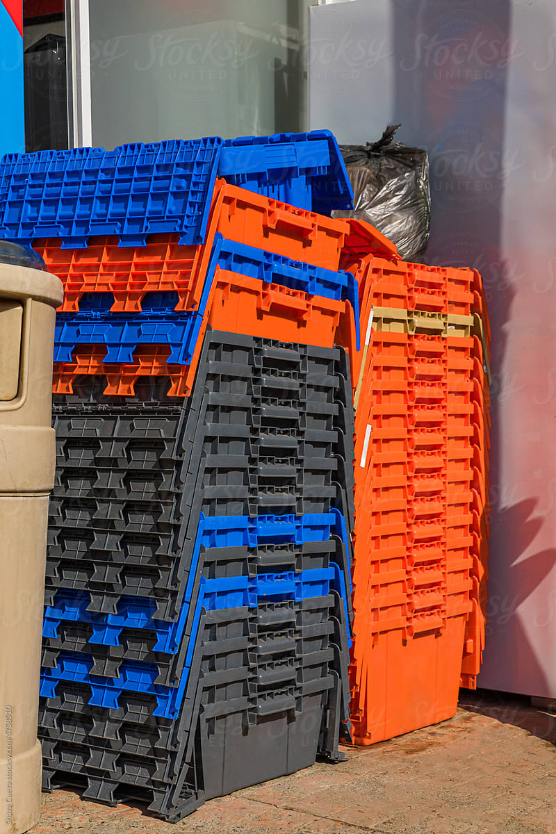 Orange and blue plastic boxes stacked next to a trash can
