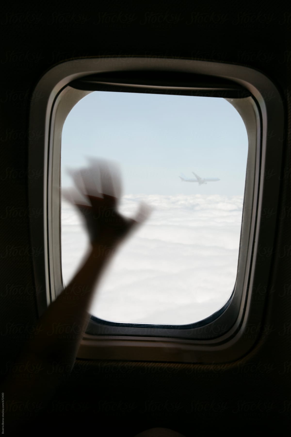 Waving hand at a window seat on an aircraft saying hello to another plane in the air