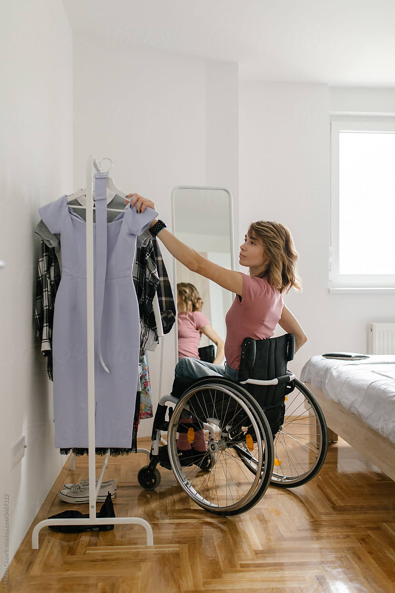 Young woman in a wheelchair choosing clothes from a clothes rack in her bedroom