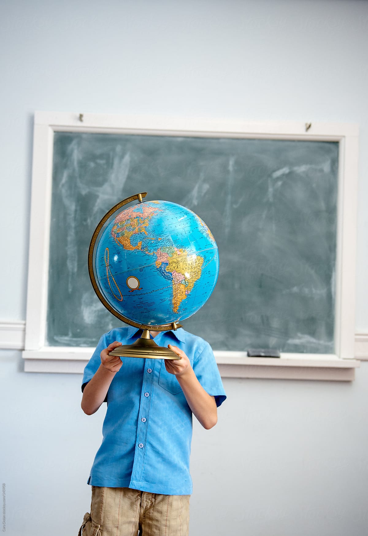 Student standing in classroom holds a globe up, covering his face