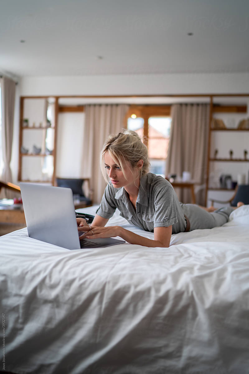 Woman relaxing on bed and working on laptop