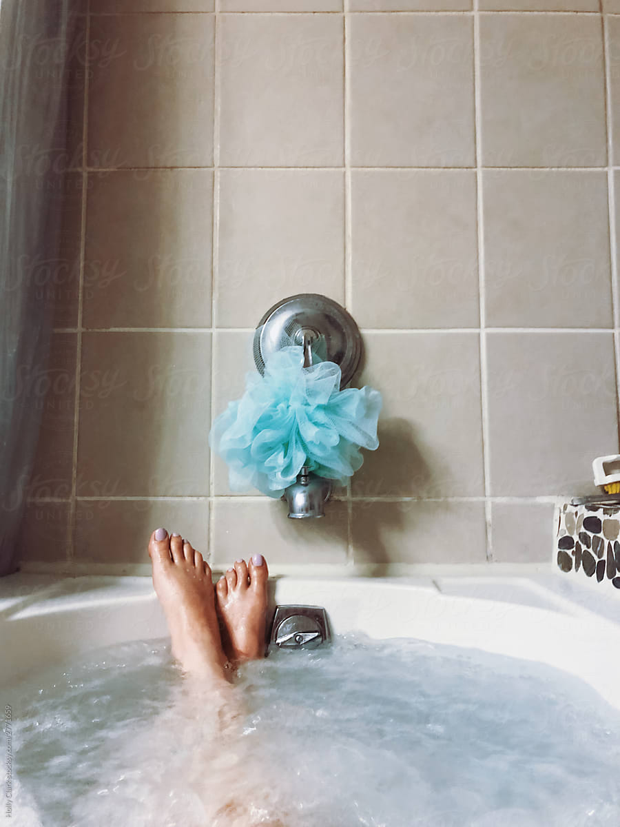 Women\'s feet in bubbling tub with blue sponge on faucet