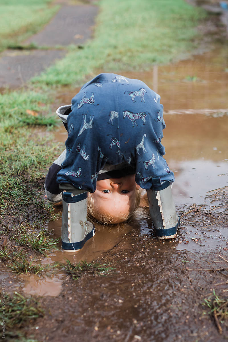 toddler boy looking through his legs in a puddle
