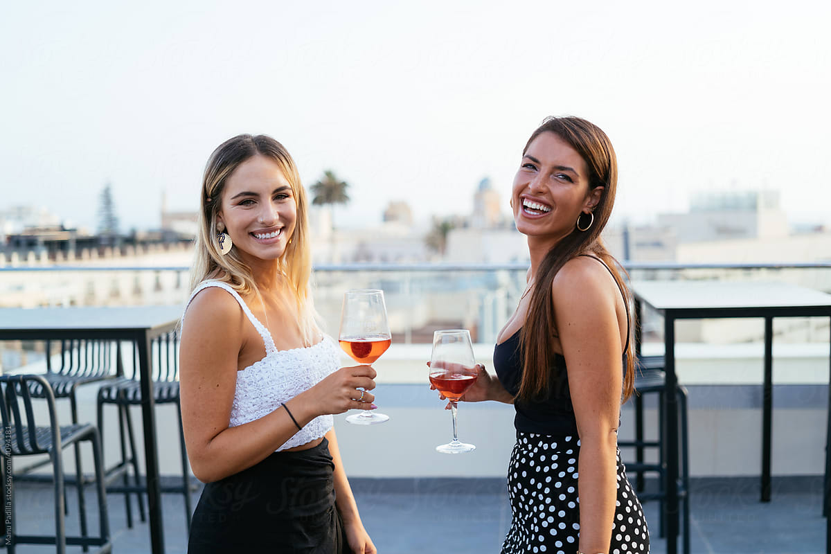 Cheerful girlfriends drinking wine on terrace