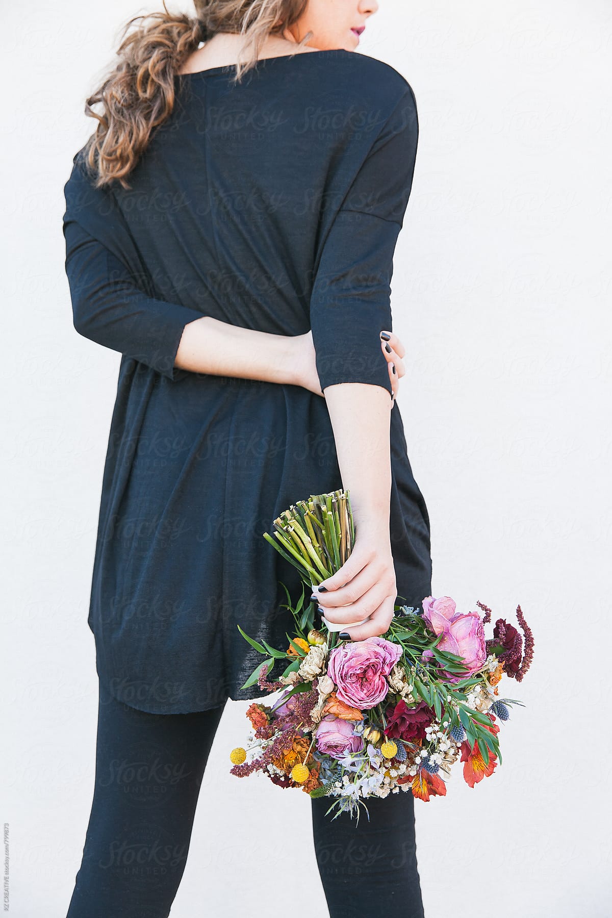 Woman wearing black holding a bouquet of wilting flowers on white background.