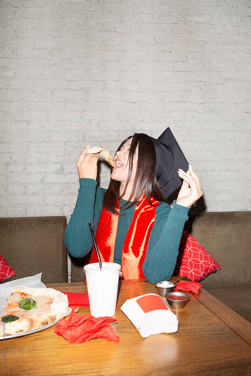 Cheerful Asian female graduate enjoying pizza in cafe