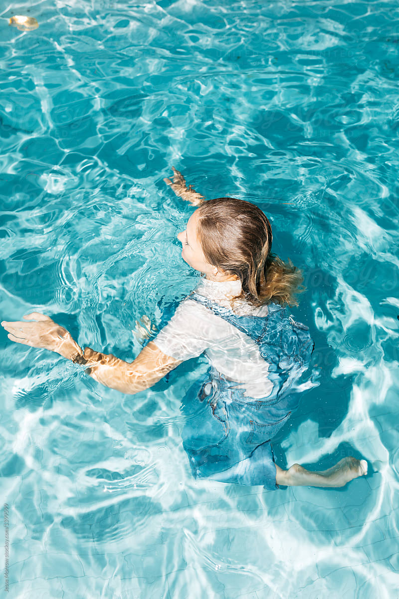 Young woman wearing all her clothes while swimming in pool during night time spontaneous summer swim