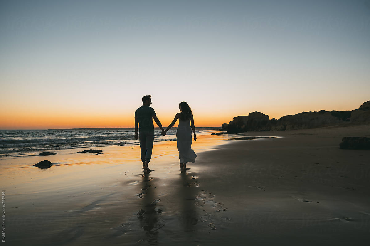 Loving couple holding hands on beach at sunset