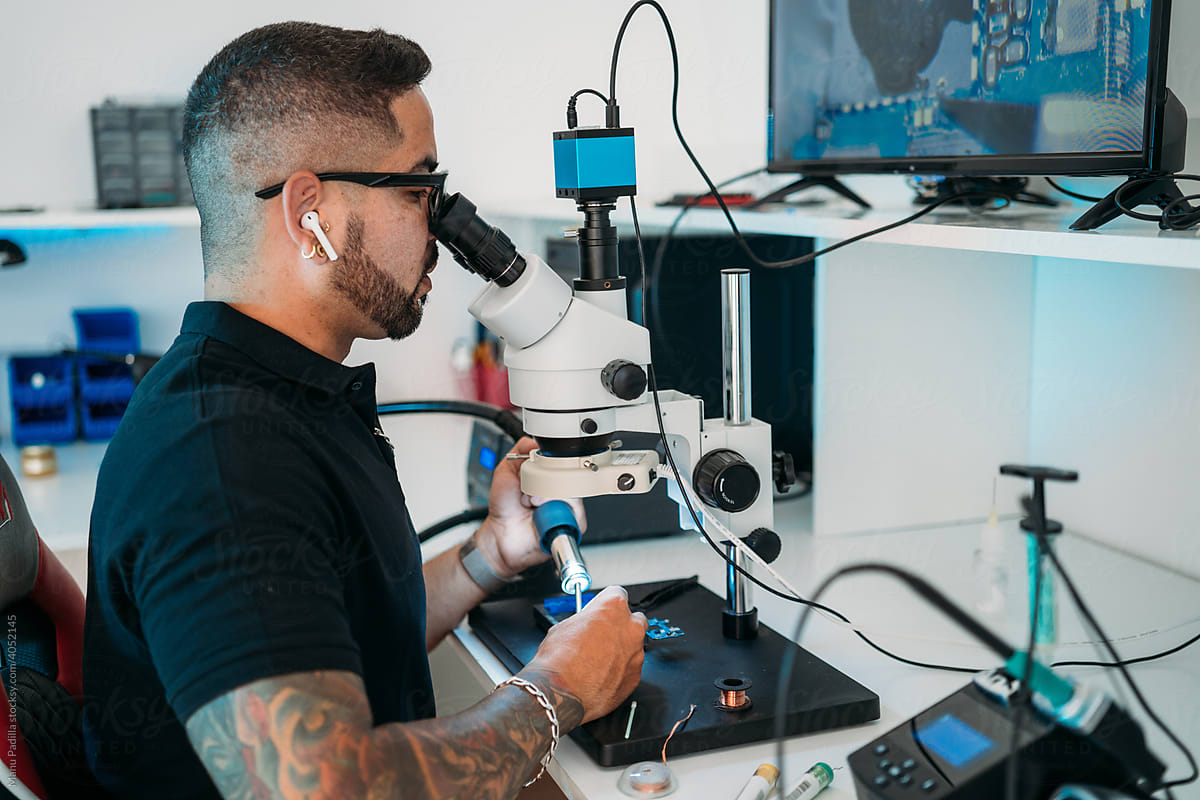 Male engineer using microscope to repair gadget