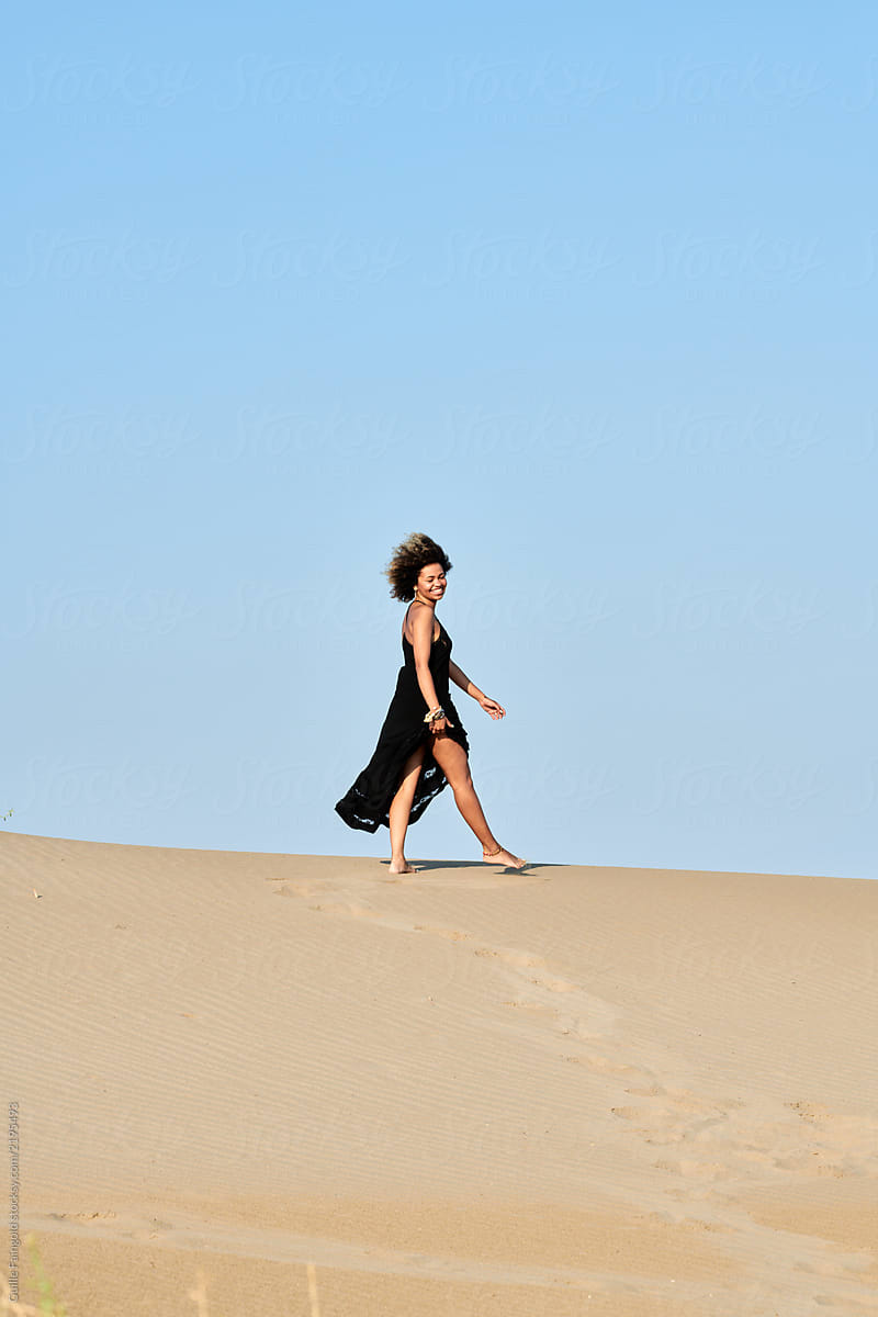 Happy woman in black dress walking on sand dune.