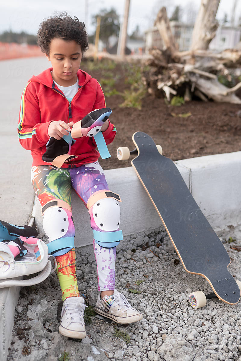 Girl with skateboard puts on elbow pads