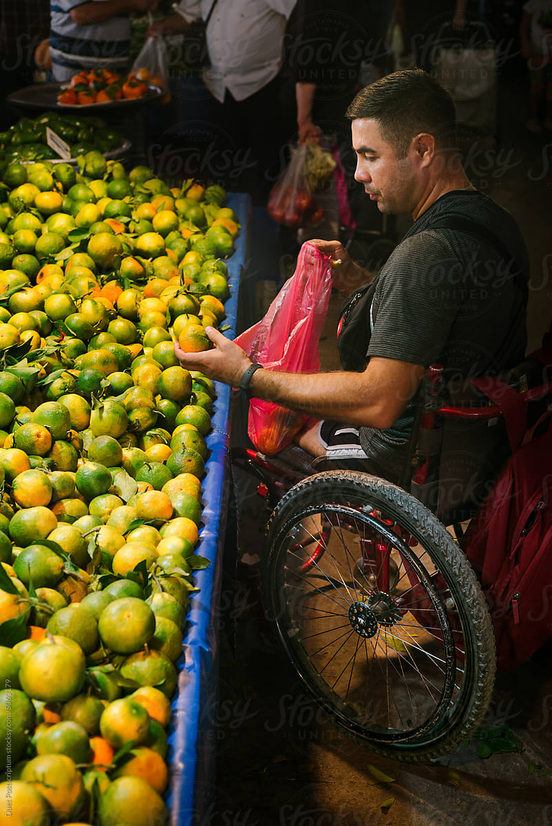 Adult man on a wheelchair chooses fresh tangerines at a street market