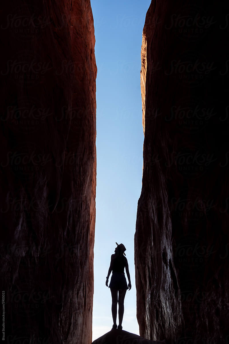A woman stands below two sandstones walls in Arches National Park