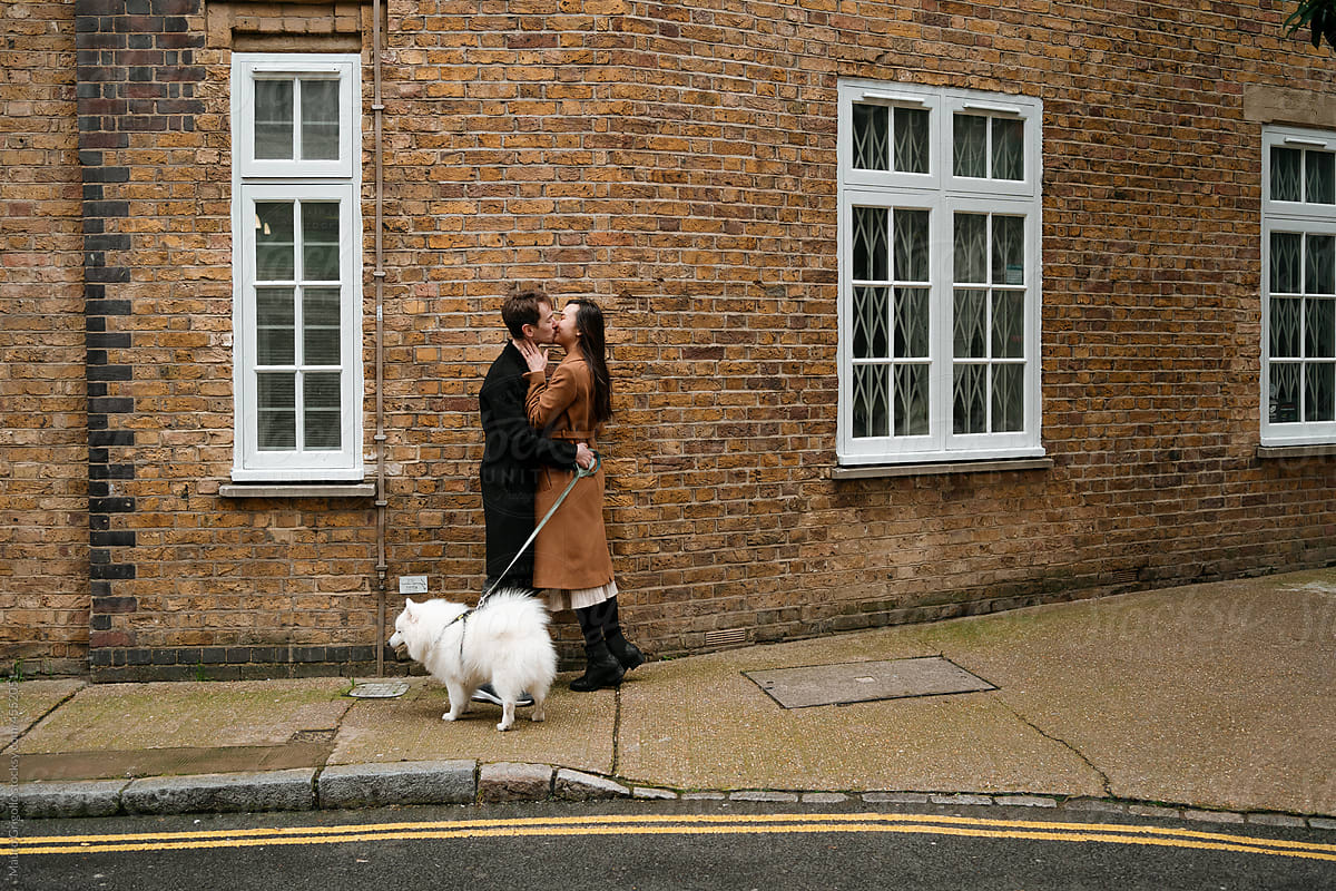 Couple kissing in the street during a walk with their dog