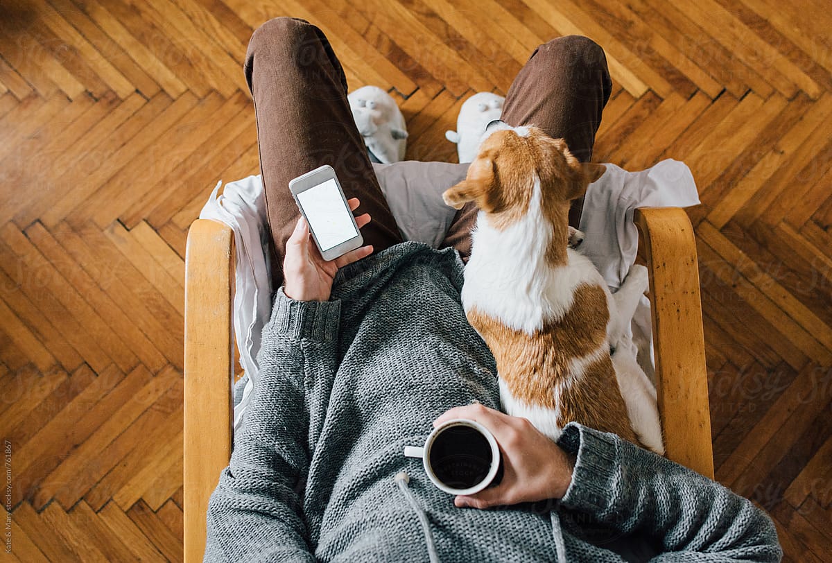 Man sitting with a dog and holding a cup of coffee and mobile phone