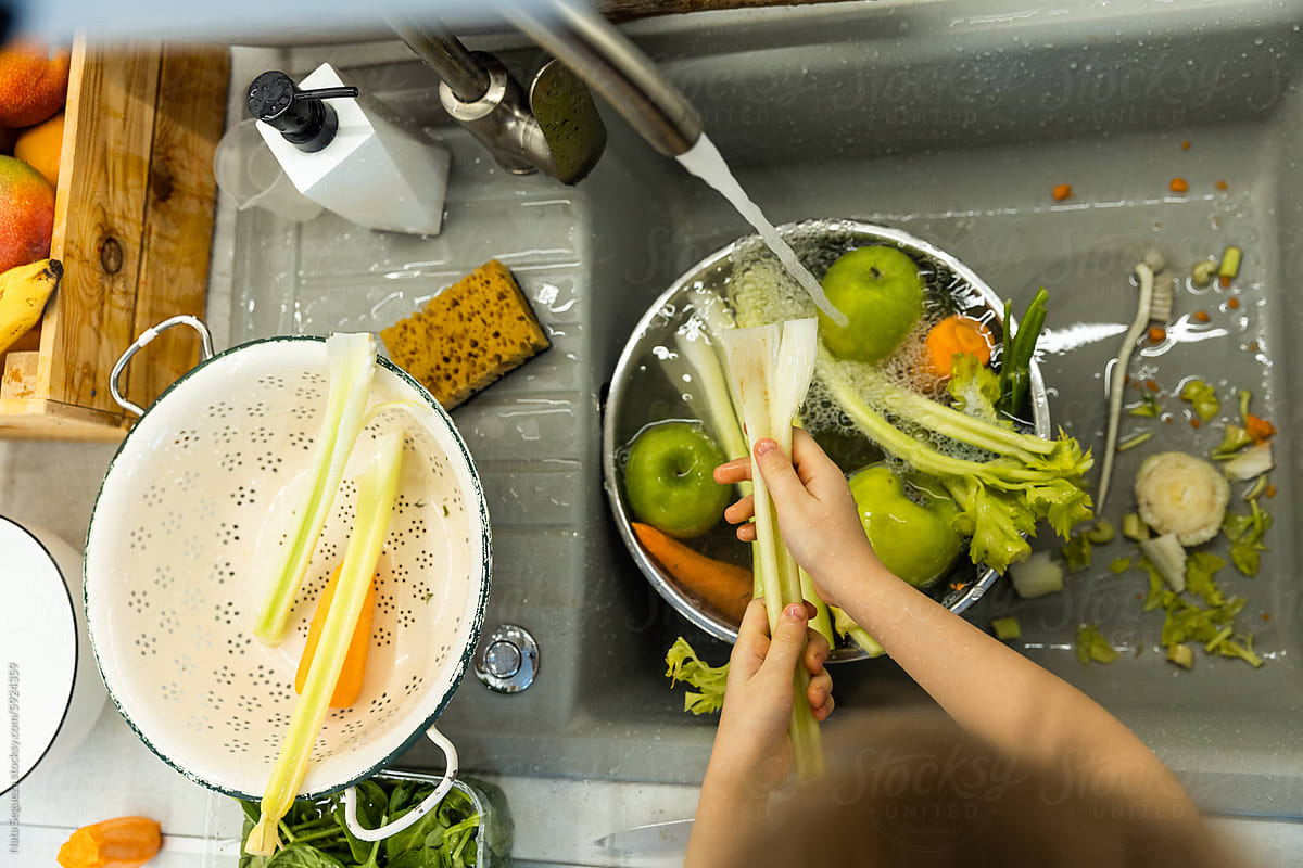 A little girl washing vegetables in the sink