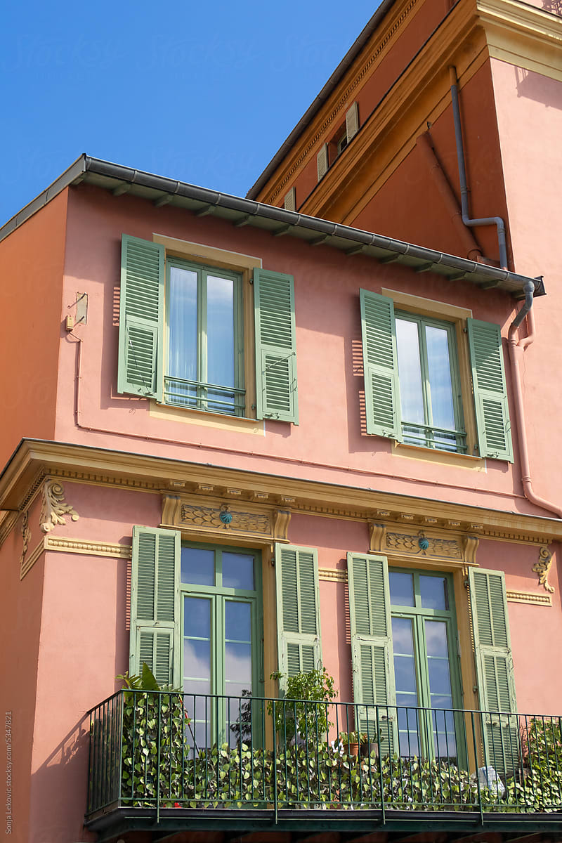 stylish pink building facade with green window shades and blue sky