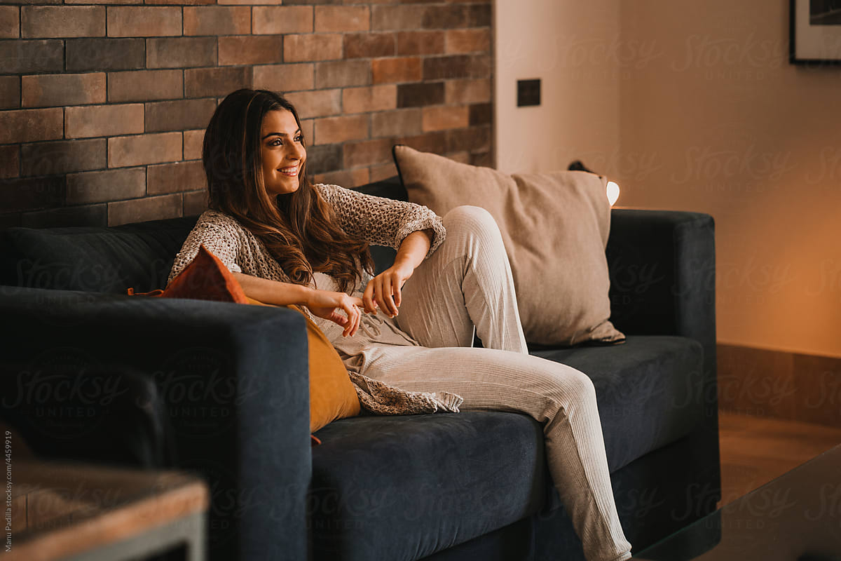 Smiling woman sitting on sofa and enjoying watching TV