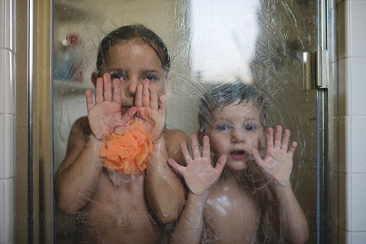 two children playing during a shower putting hands on the glass, making exp...