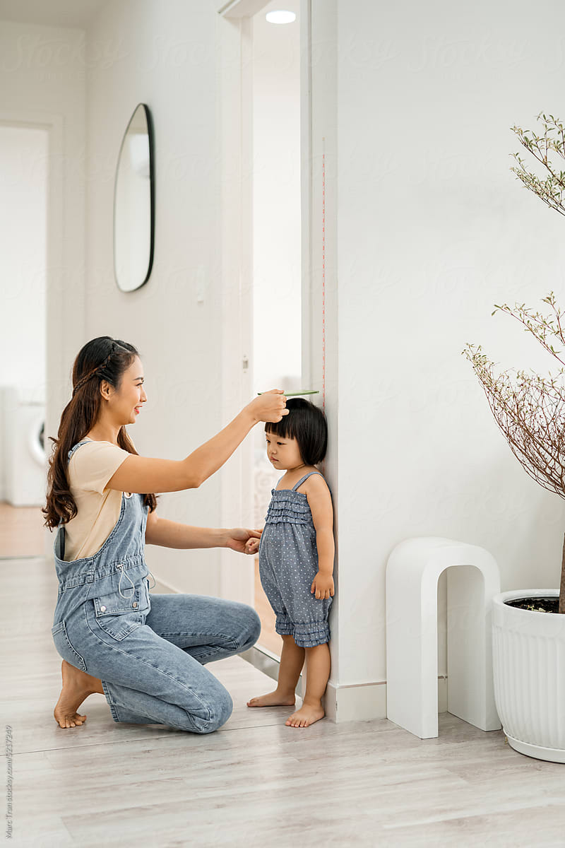 Young woman measuring her daughter\'s height indoors