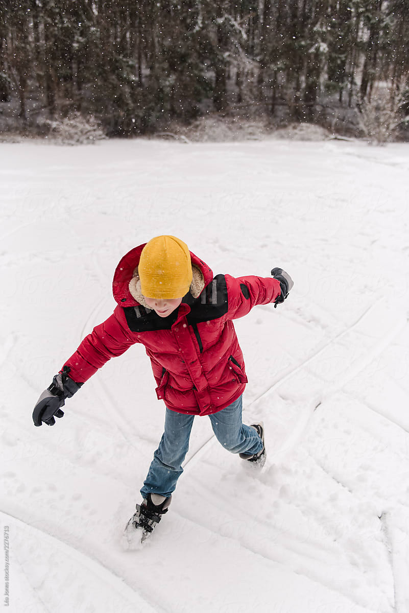 boy with red jacket skating in the snow on a frozen pond
