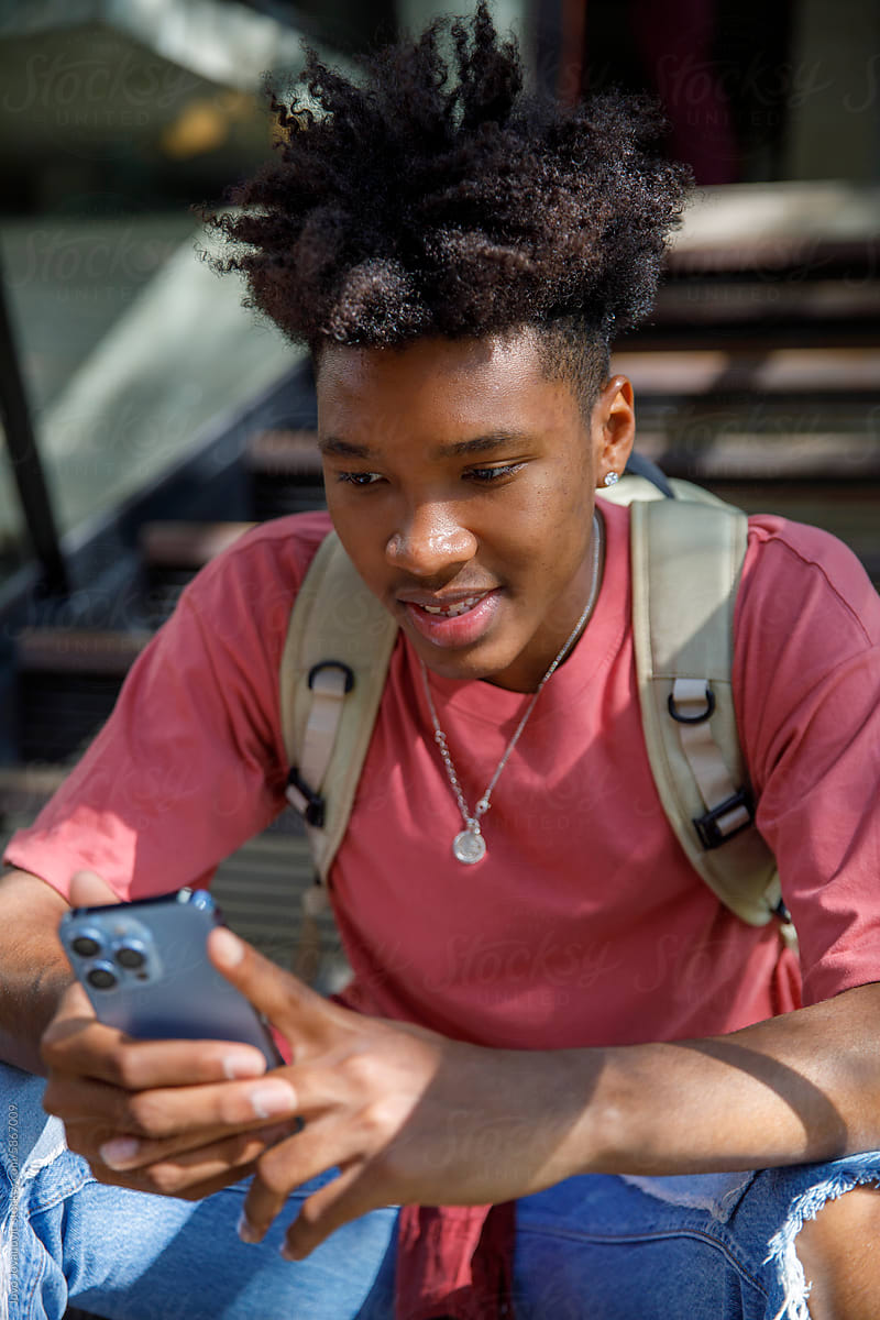 Smiling teenage boy socializing on smartphone on staircase