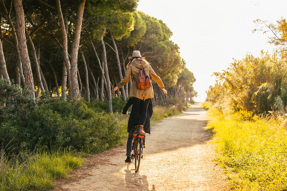 Back view of a hipster couple having fun on a bicycle in the forest.