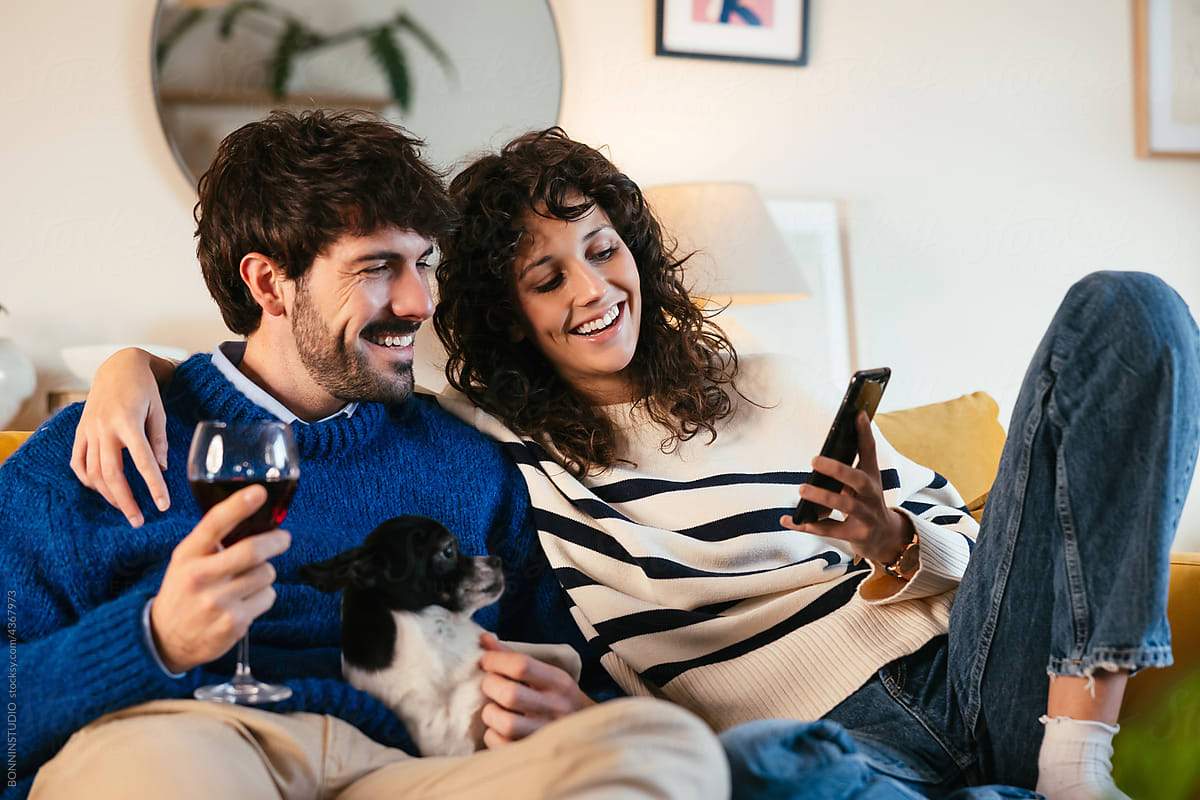 Gleeful couple with dog using smartphone on couch