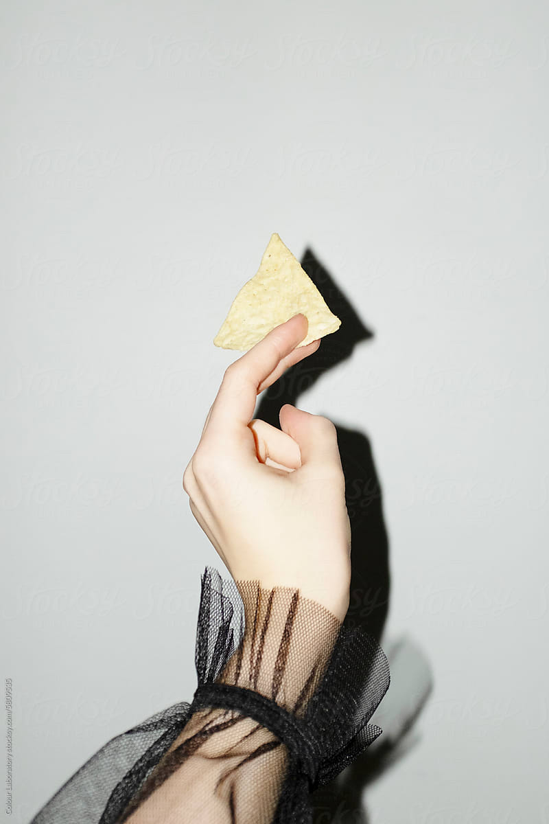Hand with elegant ruffled mesh shirt holding chip/crisp/salty snack