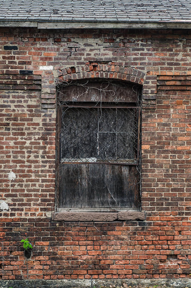 broken, boarded-up window in brick factory wall