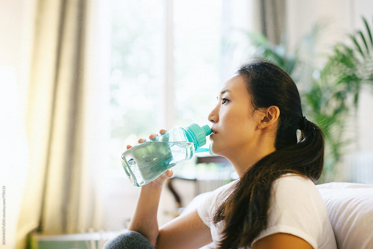 Side view of a young asian woman drinking water after doing yoga ...