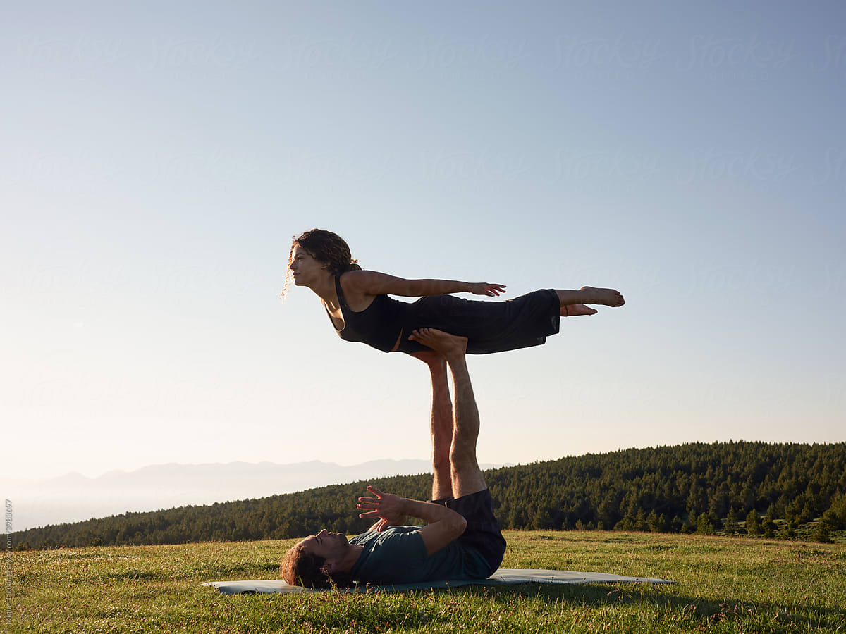 Man and woman practicing pose of acro yoga on lawn