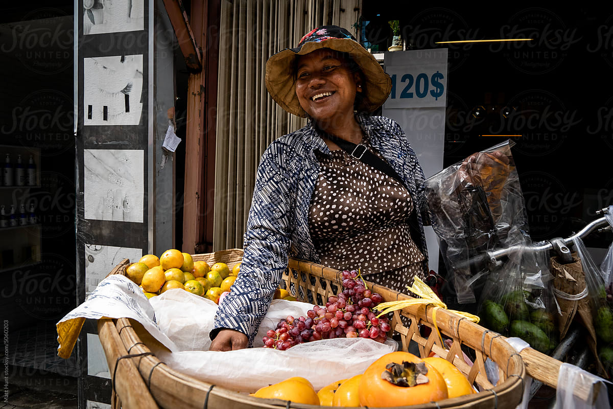 A bicycle fruit seller reaches for grapes while smiling in Cambodia