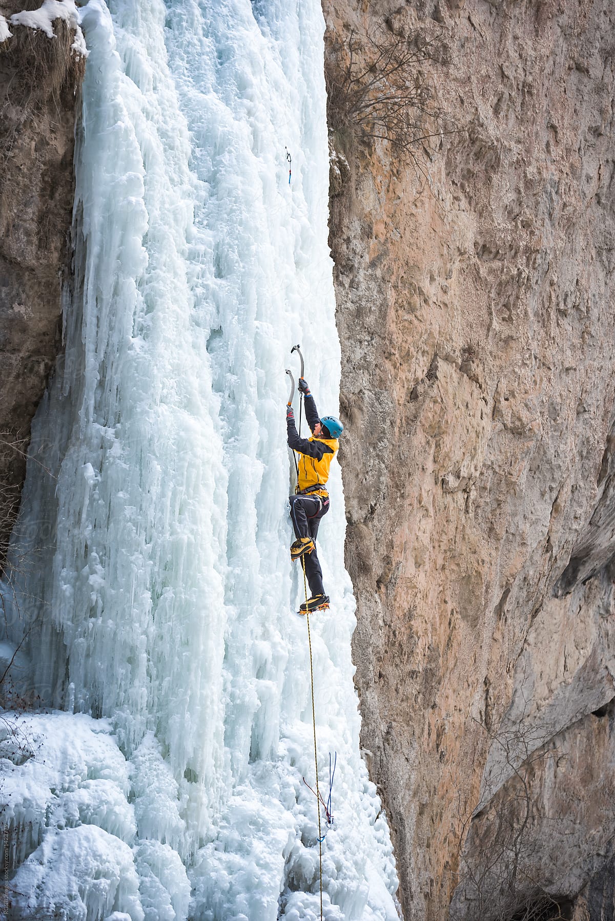 Male alpinist ice climbing on steep frozen waterfall