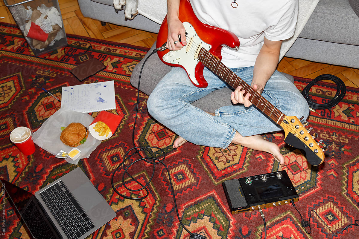 Crop man playing electric guitar on floor