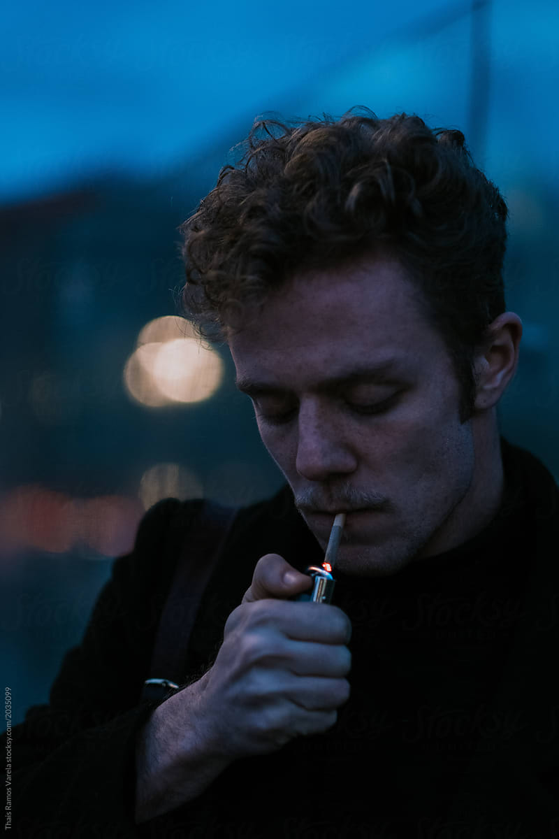 portrait of a stylish young man on the blue city ighting a cigarette