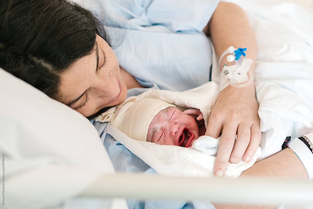 Mother and crying newborn baby sleeping on hospital bed