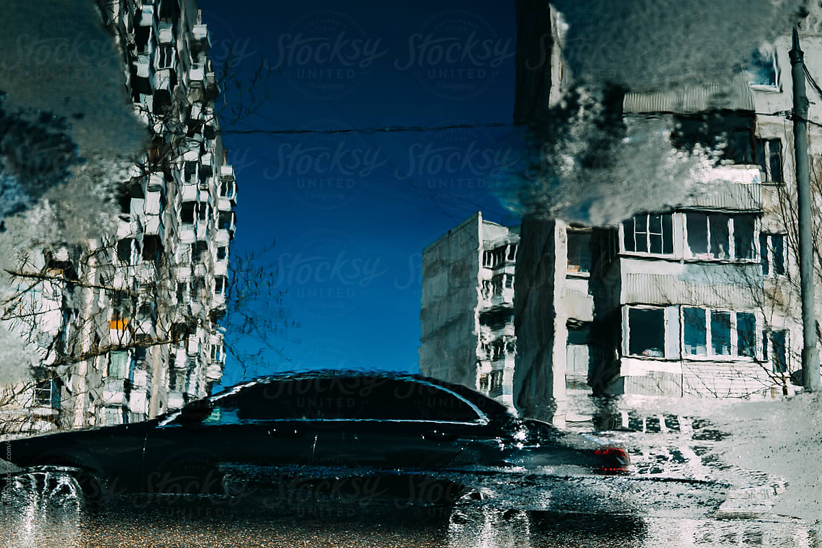 Reflection of apartment buildings and a car in a puddle.
