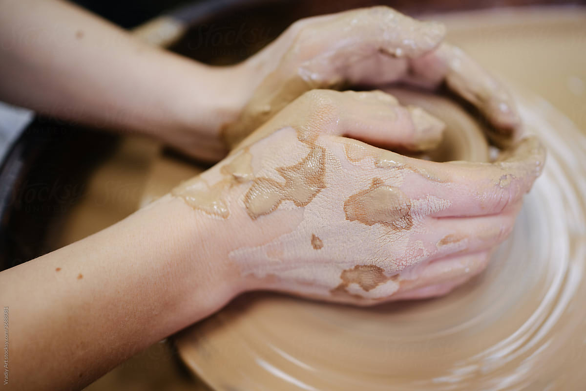 Closeup hands of pottery artist in clay on workshop