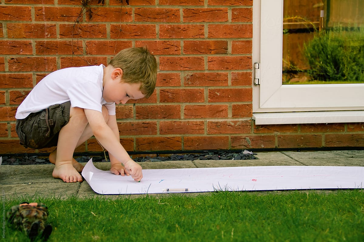 A boy draws on a roll of paper in the garden
