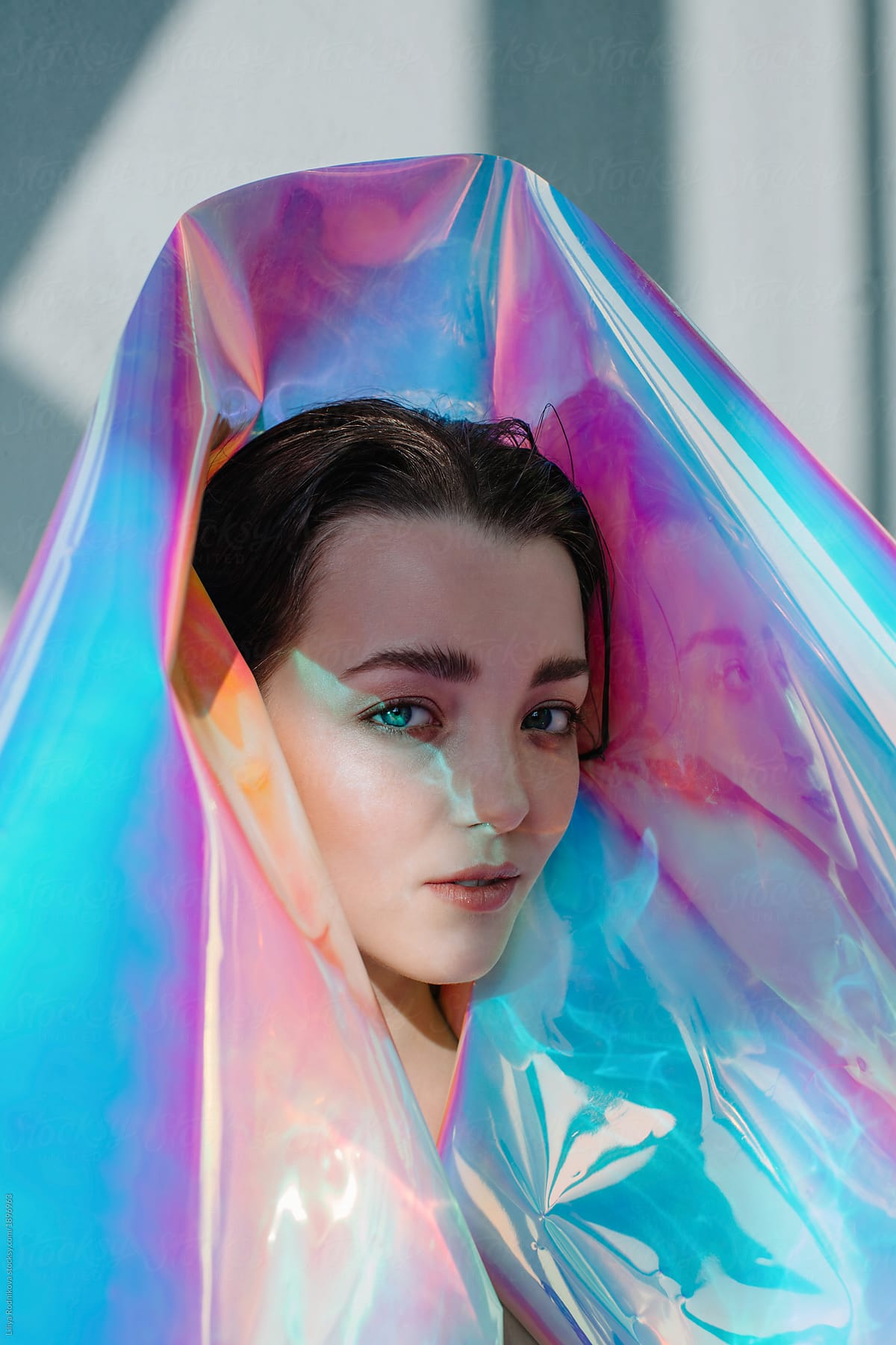 Futuristic portrait of young attractive female with weird light on her face wrapped with holographic foil